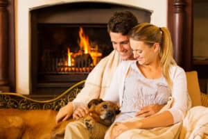 A young couple sitting by a fire with their dog. 