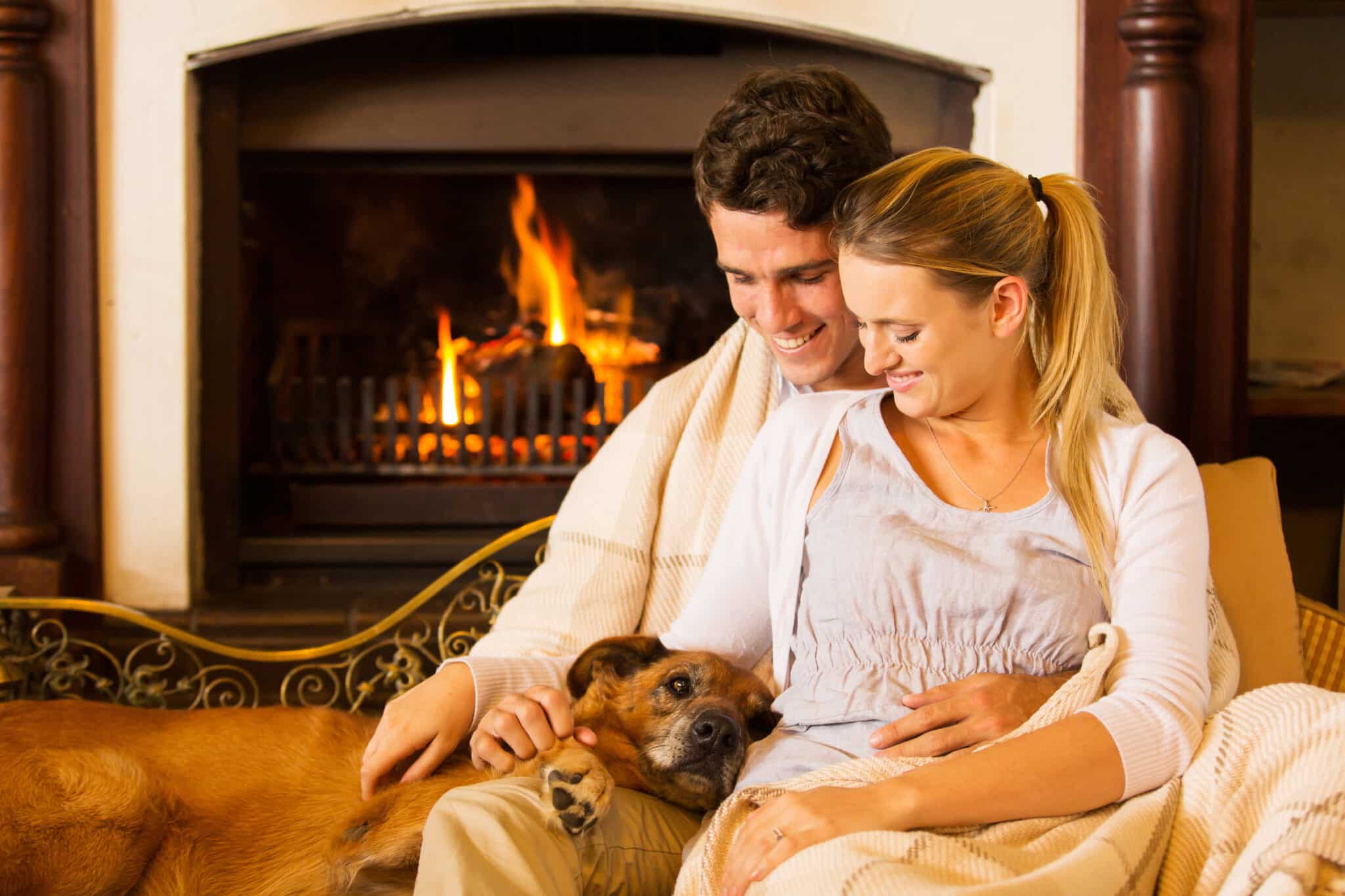 Young couple sitting by fireplace with their pet dog.