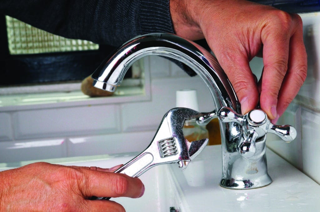 Person using a wrench to tighten a chrome bathroom faucet while adjusting the handle with their other hand.